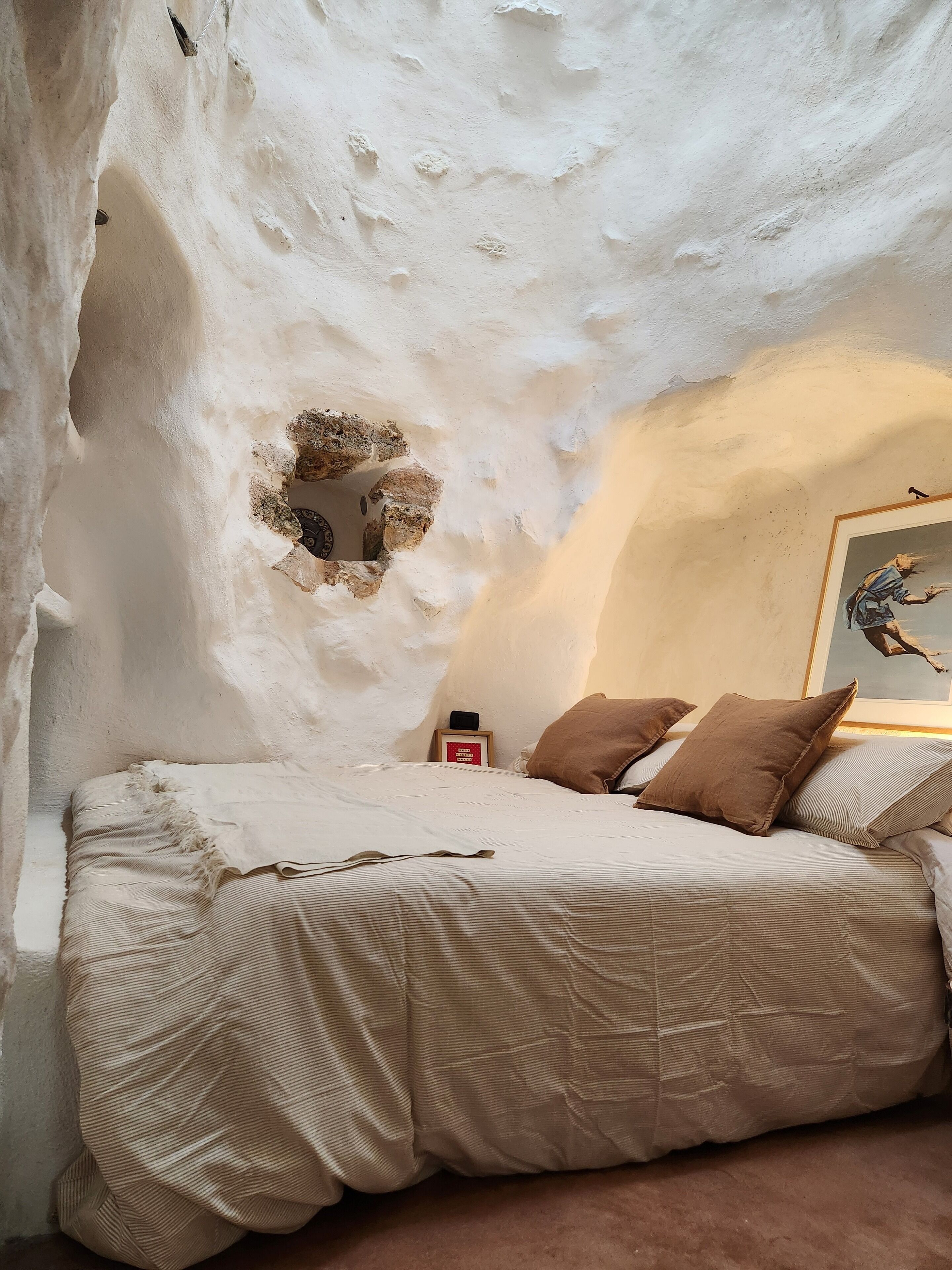 Un dormitorio acogedor con cama, almohadas, un cuadro enmarcado y una mesita con un libro.