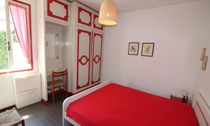 A bedroom with a red bedspread, a wooden chair, a desk, and a wardrobe with red accents. - Green oasis in Lignano Pineta (Lignano Sabbiadoro)