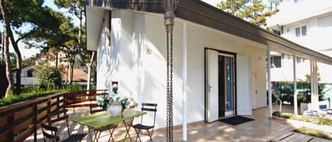A patio with a table and chairs, a hanging light fixture, and a door leading to a covered area.