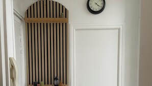 A white door with a black and white striped shelf above it, a wall clock, and a small table with a framed picture and candle. - A cocoon in the presbytery (with private parking)  (Caen)