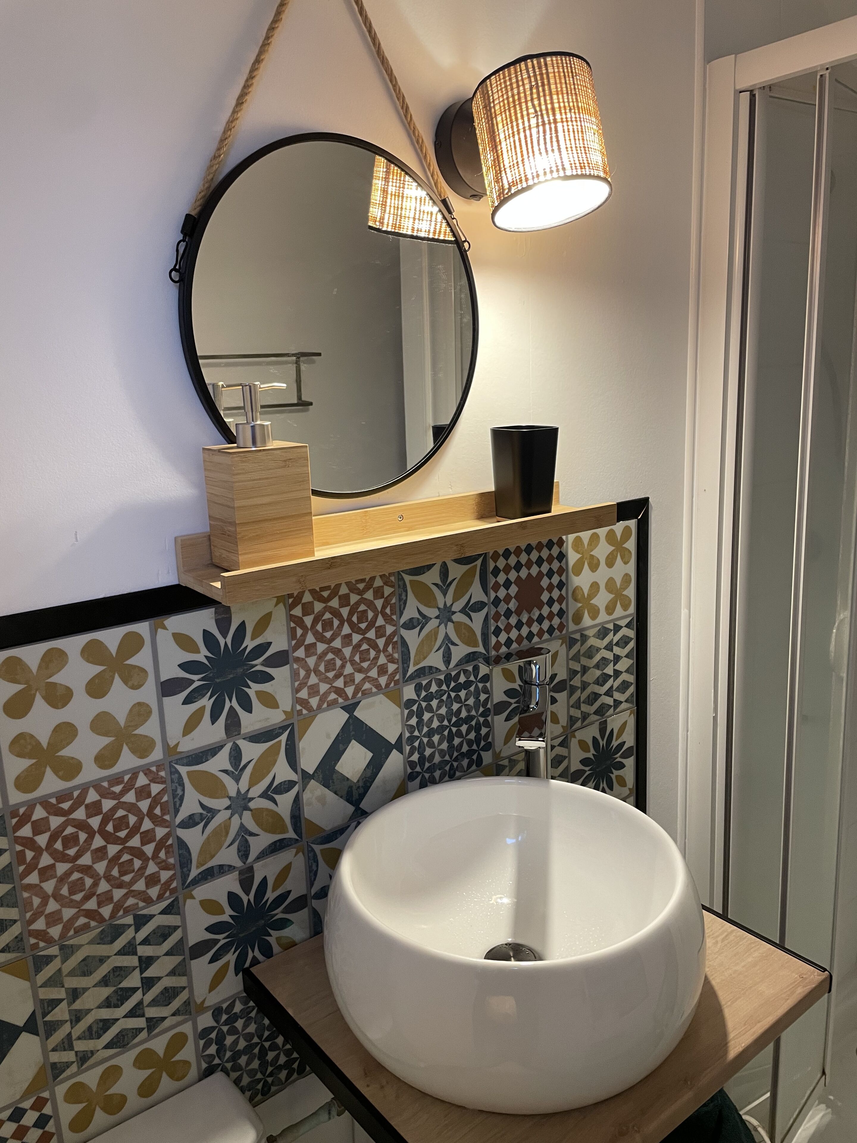 Un bagno con uno specchio tondo, un lavandino bianco e uno schienale piastrellato decorato.