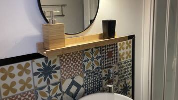 Un bagno con uno specchio tondo, un lavandino bianco e uno schienale piastrellato decorato.