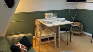 A cozy loft-style room with a slanted ceiling, a skylight, a dining area with a table and chairs, a TV mounted on the wall, and a green upholstered sofa. - A cocoon in the presbytery (with private parking)  (Caen)