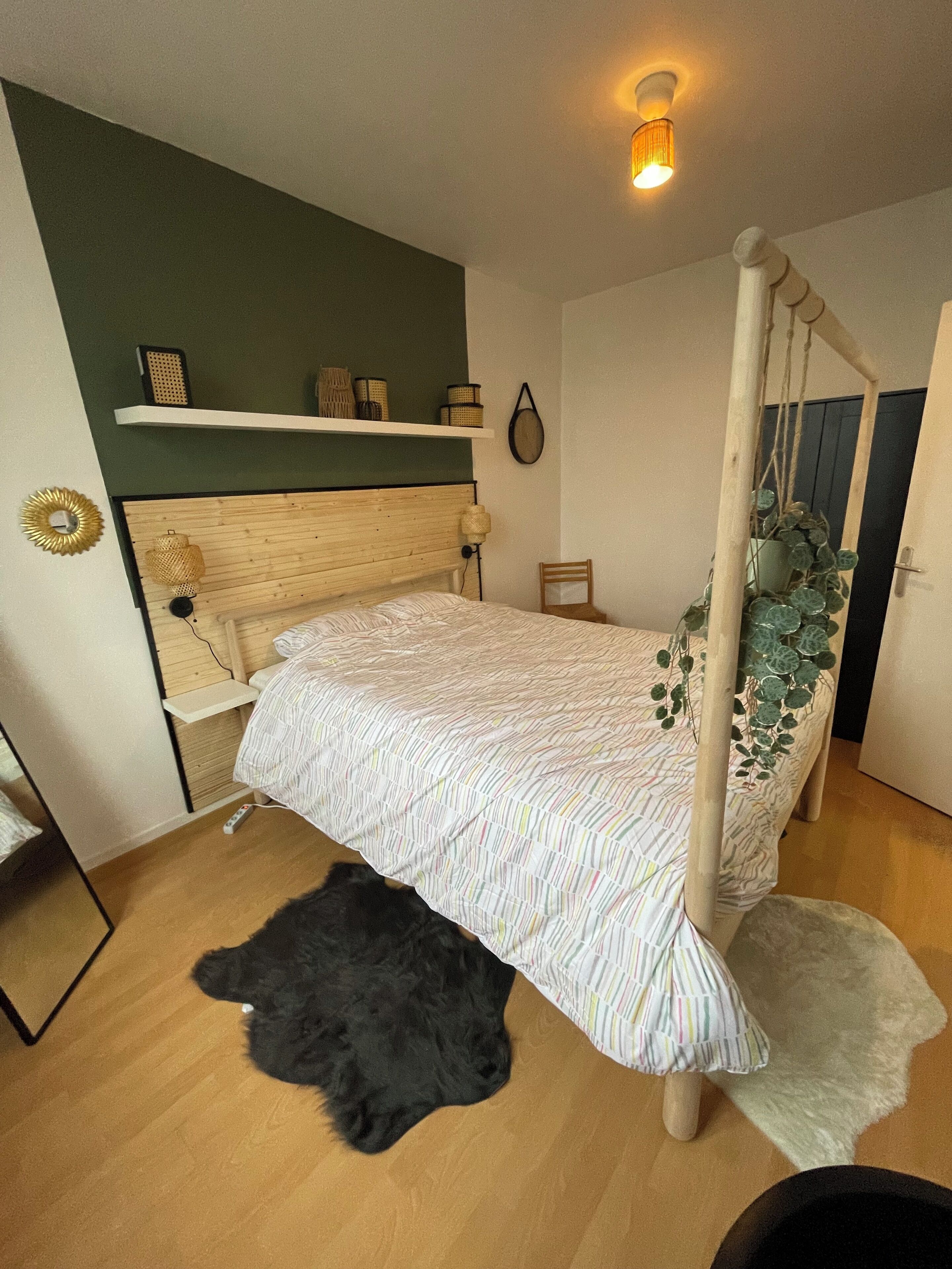 Une chambre à coucher avec un lit à baldaquin en bois, une petite table de chevet, une étagère avec des objets décoratifs, une plante suspendue et un tapis noir et moelleux sur le sol.