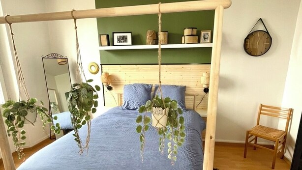A bedroom with a wooden bed frame, a hanging plant, a white rug, and a wooden chair. - A cocoon in the presbytery (with private parking)  (Caen)