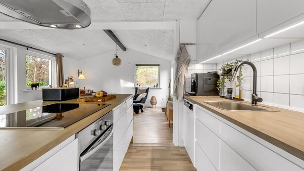 Eine moderne Küche mit einer zentralen Kochinsel, einem eingebauten Backofen und einem großen Fenster mit Blick ins Freie.