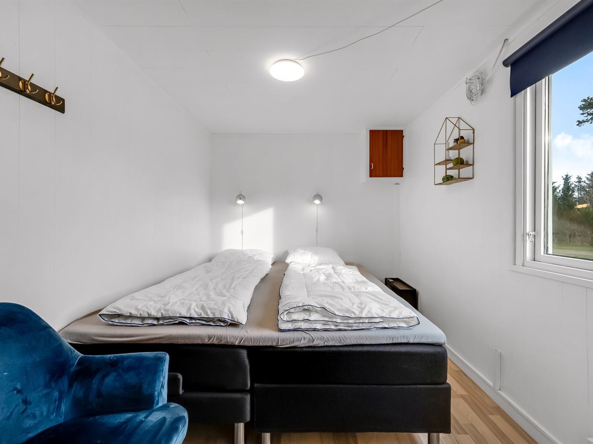 Ett sovrum med en säng, sänglampor, ett fönster och en blå stol.