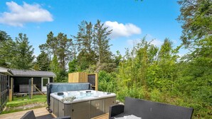 Ein Whirlpool auf einer Holzterrasse mit Korbmöbeln und einem kleinen Tisch.