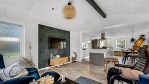 Ein modernes Wohnzimmer mit einem großen Fernseher, einem Essbereich und einer Küche im Hintergrund.