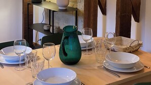 A dining area with a table set for four, featuring a green vase, white plates, and clear glasses.