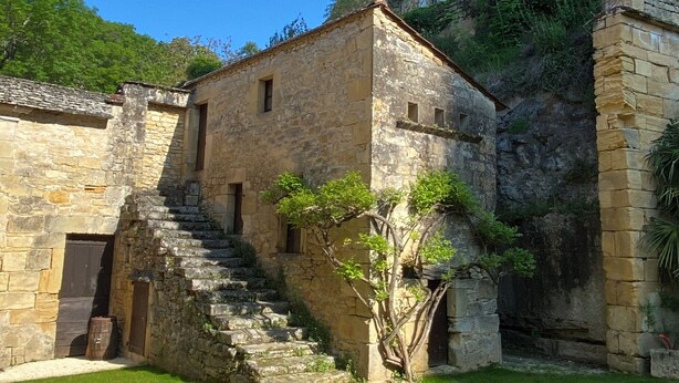 A stone building with a staircase leading to a second floor, surrounded by a grassy courtyard.