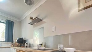 A modern kitchen with two wooden bar stools, a countertop with a kettle, a toaster, and a sink. - 45 Garden Guest Suite Studio (Bassendean)