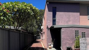 A narrow brick pathway leading to a two-story building with a purple facade. - 45 Garden Guest Suite Studio (Bassendean)