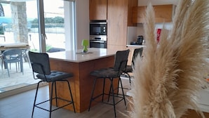 A modern kitchen with wooden cabinets, a central island with bar stools, and a view through large windows. - House Pietrosella Sea view 50 m from the beach (Pietrosella)