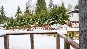 Un banc en bois, placé dans un espace extérieur enneigé, avec des arbres à feuilles persistantes et un bâtiment en arrière-plan.