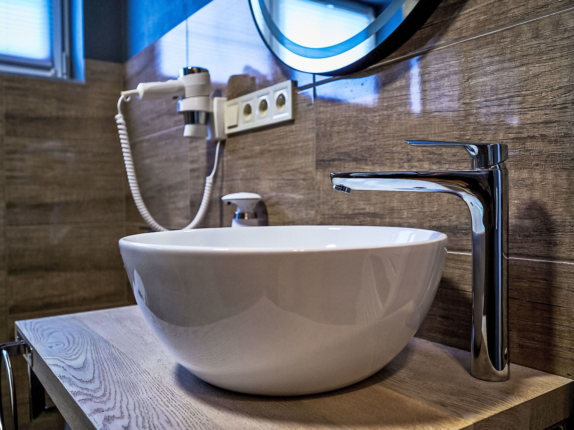 A modern bathroom with a white ceramic sink, chrome faucet, and a handheld showerhead.