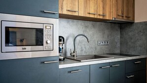 Une cuisine moderne équipée d’un four à micro-ondes encastré, d’une machine à café, d’un évier et de meubles de rangement en bois.