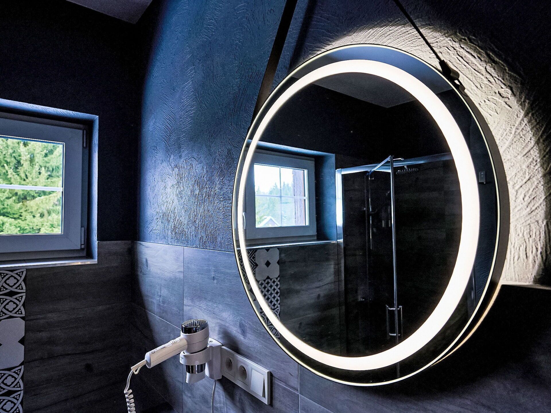 Un baño con un espejo grande, un secador de pelo y una ventana con vistas a árboles.