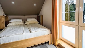 A bedroom with a sloped ceiling, a wooden bed frame, and a large window with curtains. - Cosy apartment for 2 people with WIFI, TV and terrace (Jilemnice)