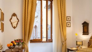 A hotel room with a bed, a table with a fruit bowl, a lamp, and a view of a stone building through the window. - Beautiful apartment for 4 people with A/C, WIFI and TV (Florence)