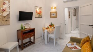 A living room with a TV, artwork, a dining table with fruit, and a sofa. - Beautiful apartment for 4 people with A/C, WIFI and TV (Florence)