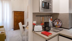 A compact kitchen with a microwave, coffee maker, and toaster. There's a wooden cabinet and a white chair in the adjacent dining area. - Beautiful apartment for 4 people with A/C, WIFI and TV (Florence)