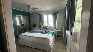 Une chambre à coucher avec un lit, un ventilateur de plafond, une fenêtre avec des rideaux et une vue sur l’extérieur.