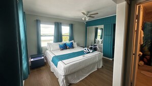 Une chambre à coucher avec un lit, un ventilateur de plafond, une fenêtre avec des rideaux et une vue sur l’extérieur.