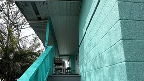 Un escalier avec des rampes de couleur turquoise menant à un espace abrité doté d’un plafond et de luminaires fixés au mur.