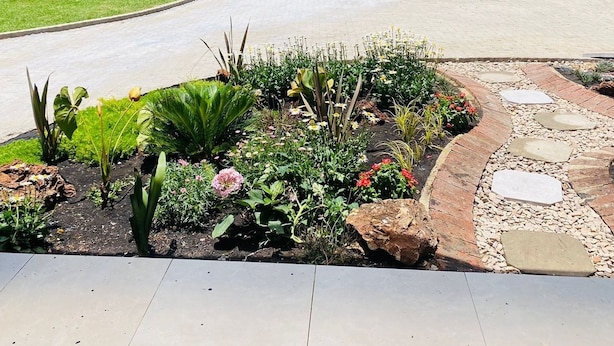 A landscaped driveway with a curved path, potted plants, and a garden area with various flowers and shrubs. - The Residence Hills Lodge (Harare)