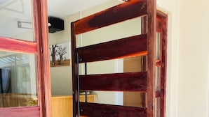 A wooden sliding door with a glass panel, leading to a room with a tiled floor and a wooden cabinet. - The Residence Hills Lodge (Harare)