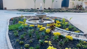 A landscaped garden with a central fountain, surrounded by a variety of plants and a paved walkway. - The Residence Hills Lodge (Harare)