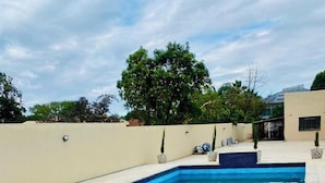 A rectangular swimming pool with blue tiles, surrounded by a beige wall and a tiled deck. - The Residence Hills Lodge (Harare)