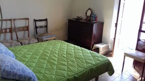 Quarto com colcha verde acolchoada, cómoda de madeira, cadeira e mesa pequena.
