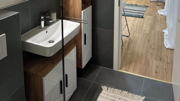Ein modernes Badezimmer mit einem weißen Waschbecken, Holzschränken und einem Spiegel.