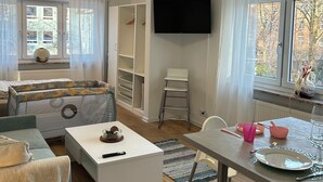 Ein modernes Wohnzimmer mit einer Couch, einem Couchtisch, einem an der Wand montierten Fernseher und einem Essbereich mit Tisch und Stühlen.