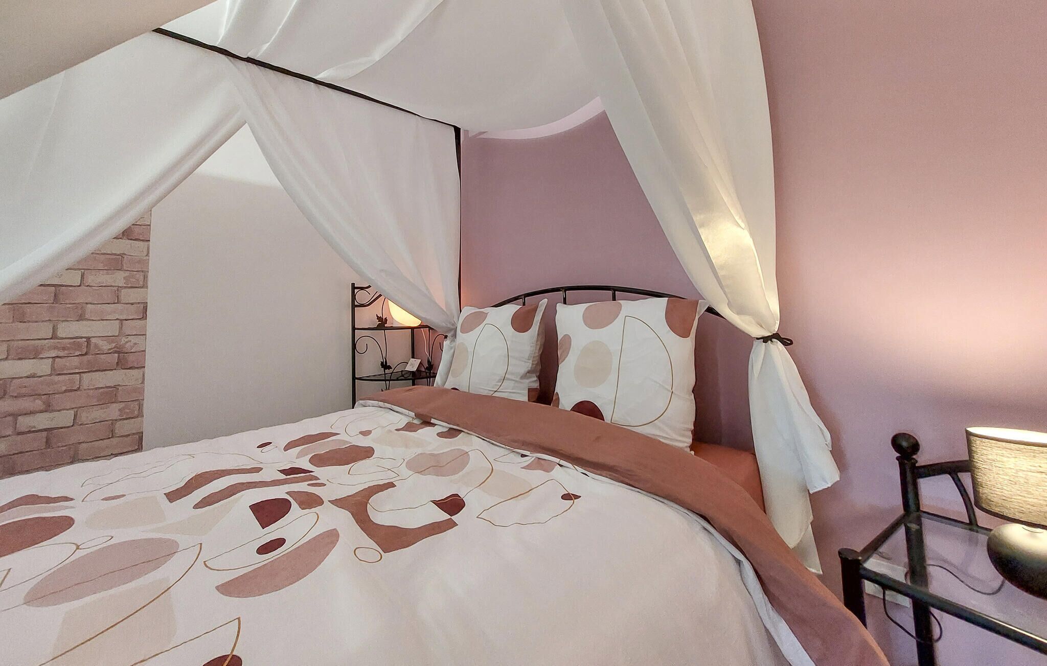 A bedroom with a canopy bed, a brick wall, and a bedside table with a lamp.