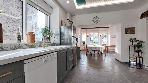 A modern kitchen with a dishwasher, a sink, and a window. There is a dining area with a table and chairs. - 4 bedroom beautiful home in Neuilly le Vendin (Neuilly le Vendin)