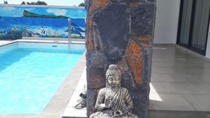 Une statue de Bouddha en pierre, placée près d’une piscine, avec une fresque représentant l’océan et des poissons en arrière-plan.
