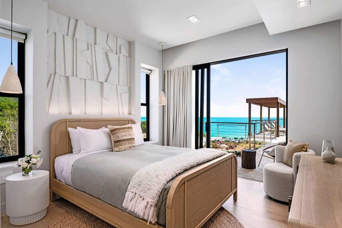 A modern bedroom with a large bed, a view of the ocean, and a balcony with outdoor furniture.