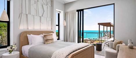 A modern bedroom with a large bed, a view of the ocean, and a balcony with outdoor furniture.