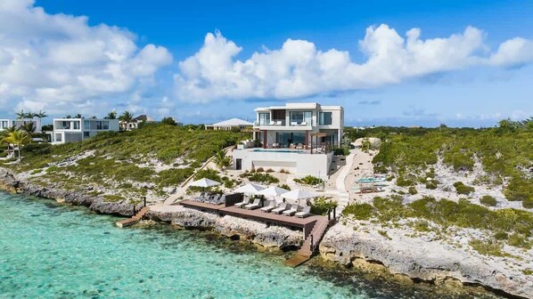 A modern beachfront property with a pool, lounge chairs, and a view of the ocean.