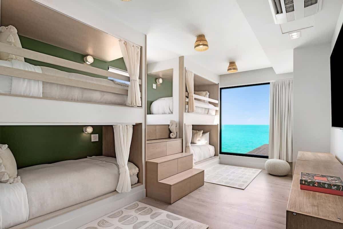 A hotel room with bunk beds, a large window with a view of the sea, a small seating area, and a TV.
