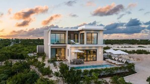 Une maison moderne à deux étages avec une piscine, entourée de verdure.