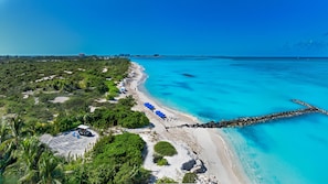 A coastal area with a beach, clear blue waters, and a rocky breakwater.