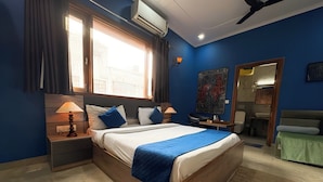 A hotel room with a large bed, two bedside tables with lamps, a window with curtains, a ceiling fan, and a bathroom visible through an open door. - Haven Hotel Sector 31,Gurugram (Gurugram)