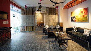 A modern living room with a sofa, coffee table, and decorative pillows. There are ceiling fans and a painting on the wall. - Haven Hotel Sector 31,Gurugram (Gurugram)
