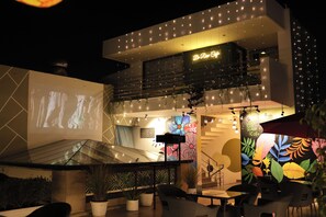An outdoor seating area with tables and chairs, a staircase, and a wall with a floral mural. - Haven Hotel Sector 31,Gurugram (Gurugram)
