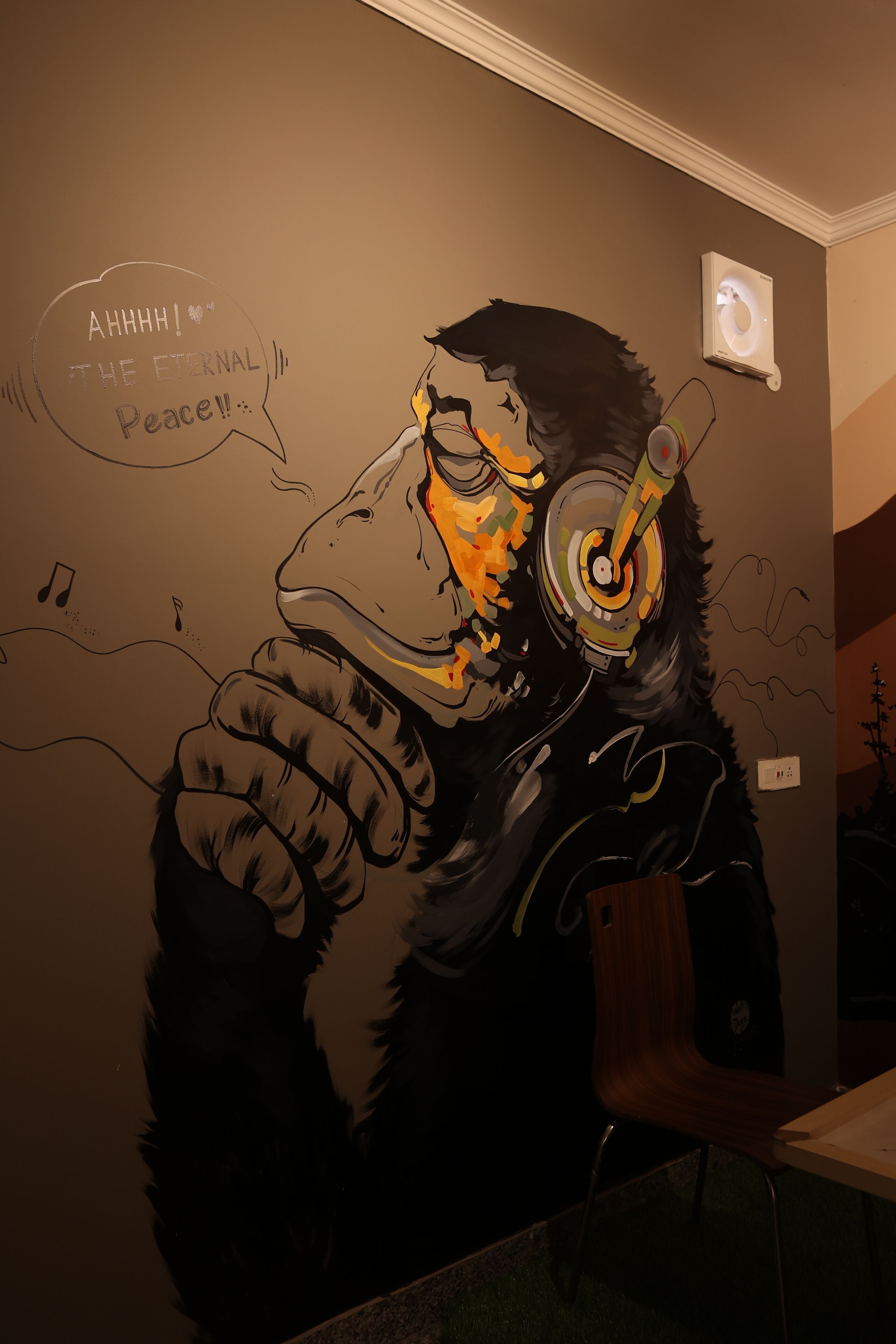A mural of a person with headphones, a speech bubble saying "AHHHH! THE ETERNAL Peace!!", and a small light fixture on the wall.