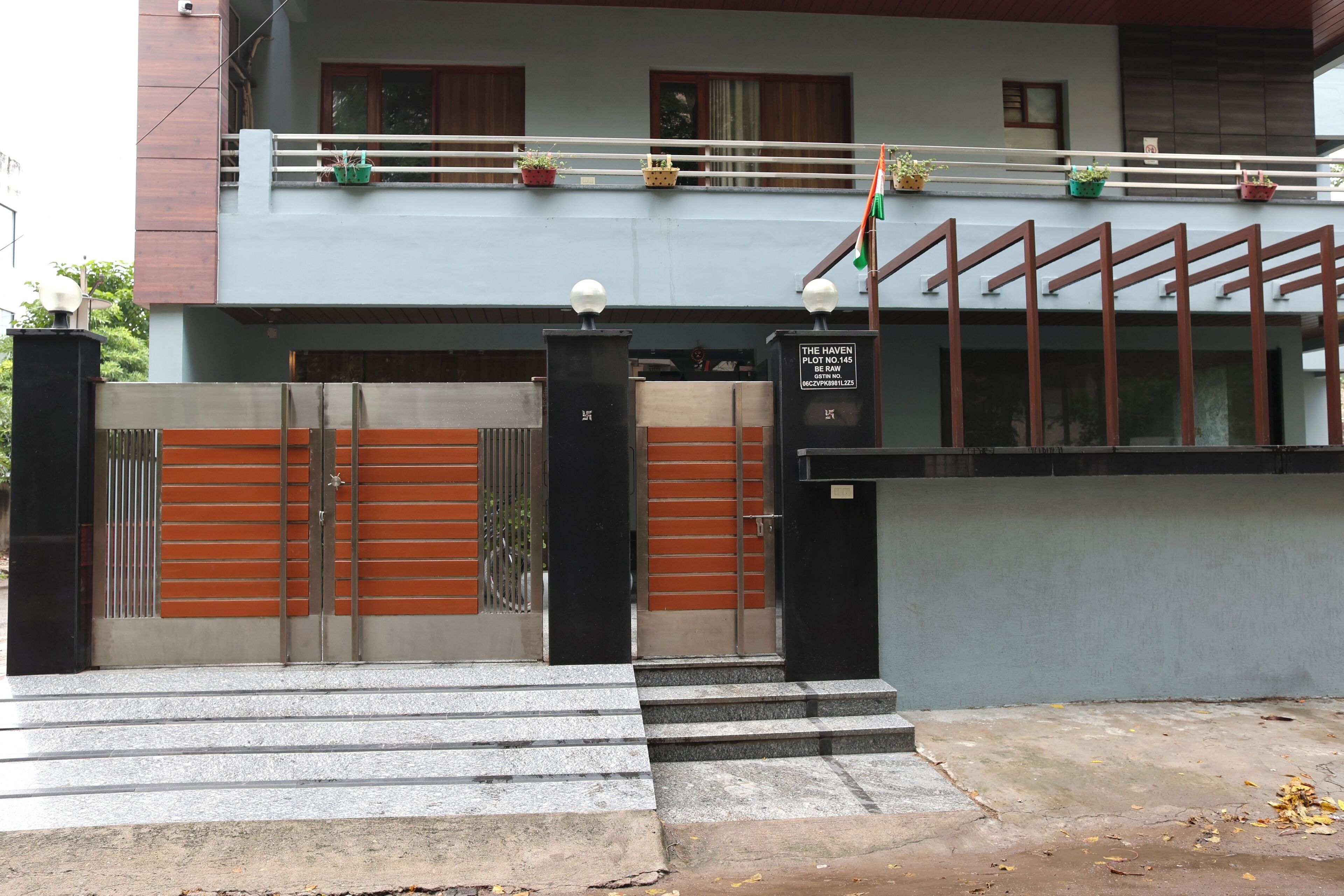 A building entrance with a gated driveway, steps leading up to the entrance, and a balcony with potted plants.